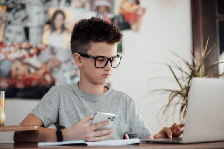 tiener aan het werk achter een laptop en op zijn telefoon