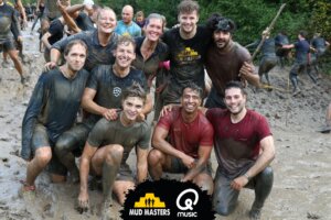 Groep enthousiaste deelnemers genieten na het voltooien van een modderig obstakelparcours, symbool voor de teamgeest en doorzettingsvermogen bij het werken bij Mud Masters.
