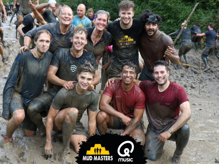 Groep enthousiaste deelnemers genieten na het voltooien van een modderig obstakelparcours, symbool voor de teamgeest en doorzettingsvermogen bij het werken bij Mud Masters.